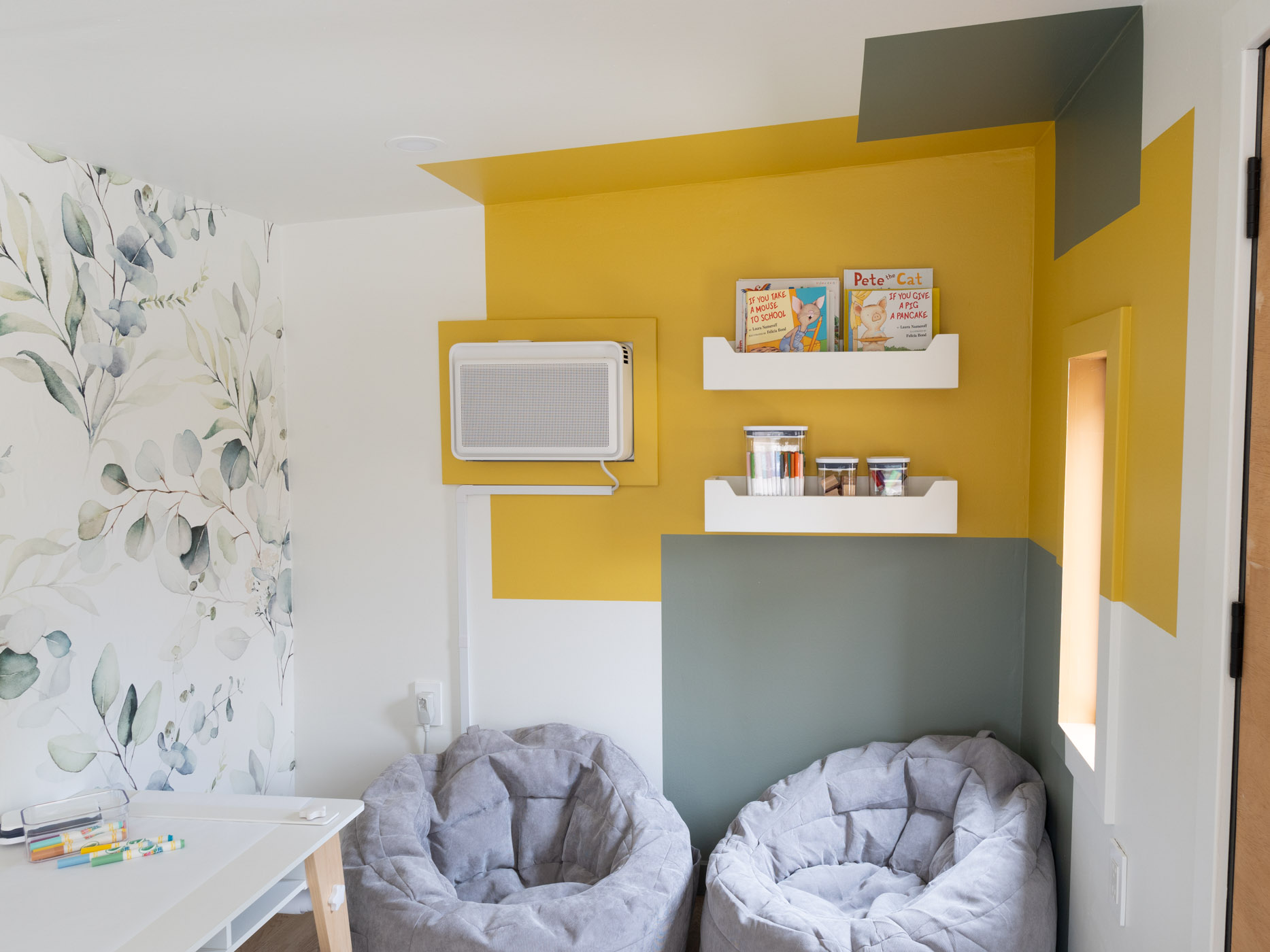 Color block wall of green and yellow with children chairs, bookshelves and table.